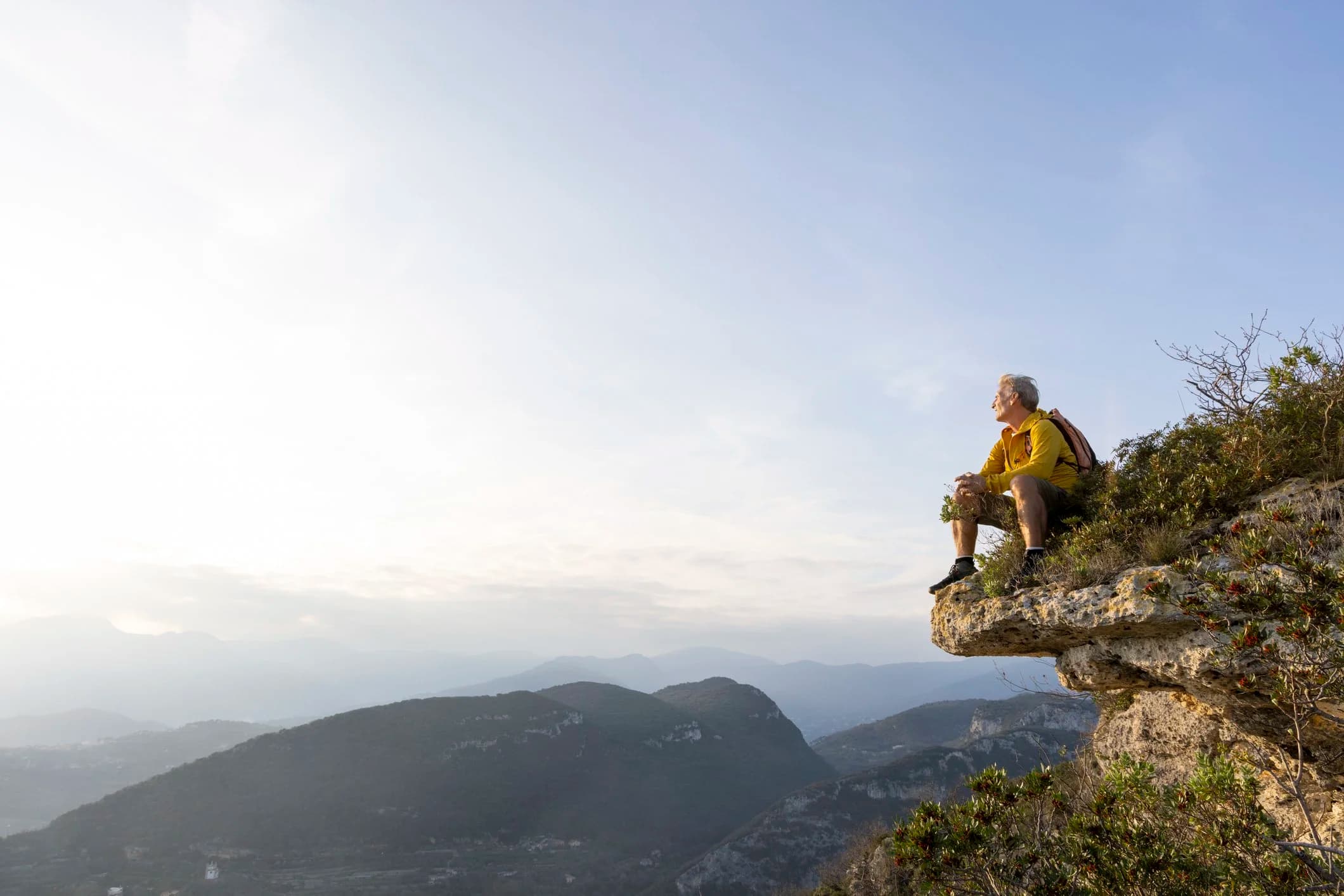 Person seated on a mountain summit looking out over an expansive landscape